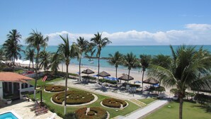 A resort with a pool, lounge chairs, palm trees, and a beach view.