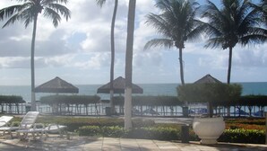 A poolside area with lounge chairs, palm trees, and a view of the ocean.