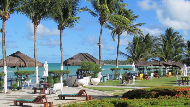 A resort with thatched-roof umbrellas, lounge chairs, and a view of the ocean.
