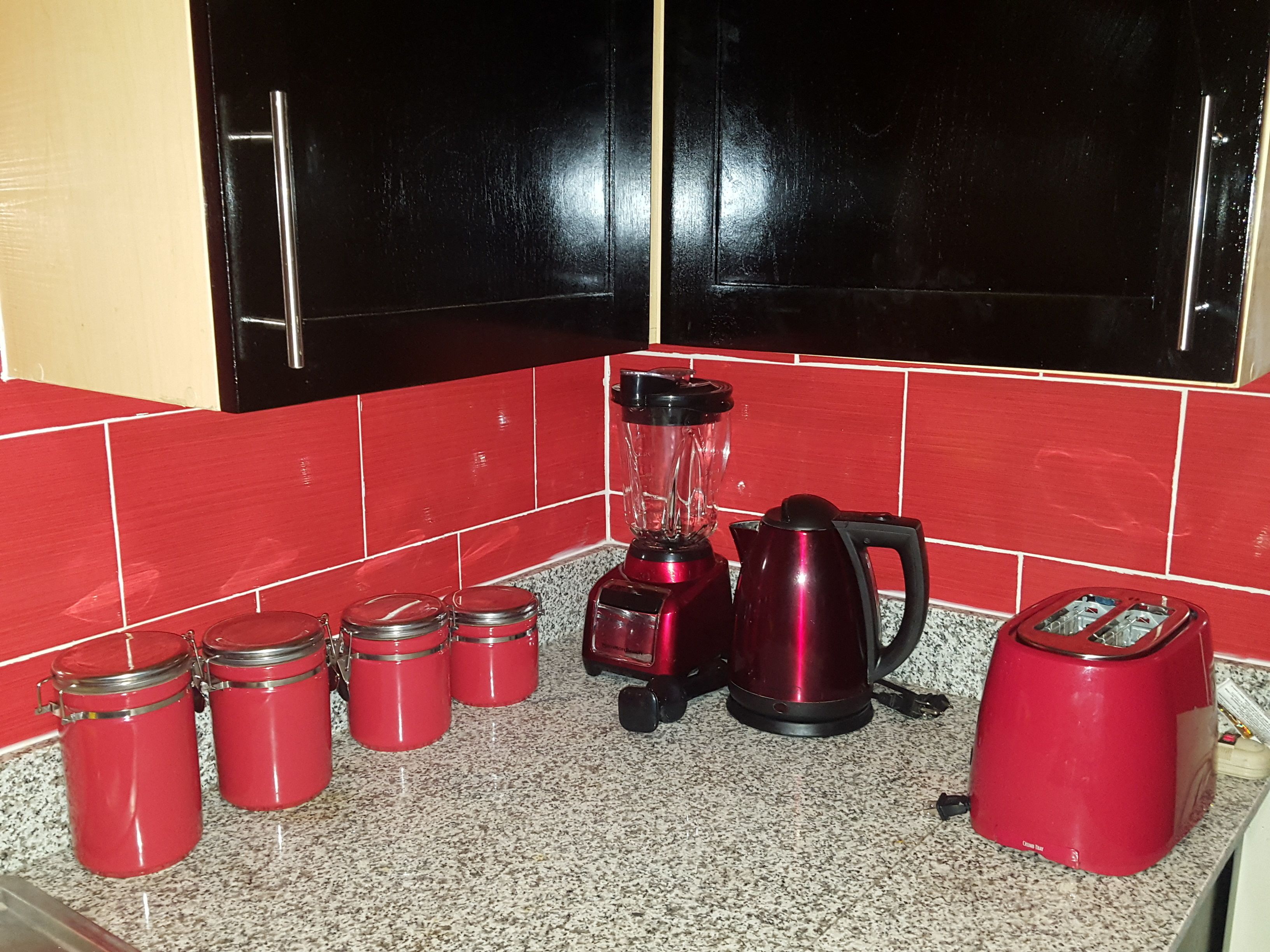 A kitchen with red appliances, including a blender, a kettle, and a toaster.