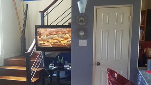 Een trap met een aan de muur bevestigde televisie, een deur met een spiegel en een rode stoel.