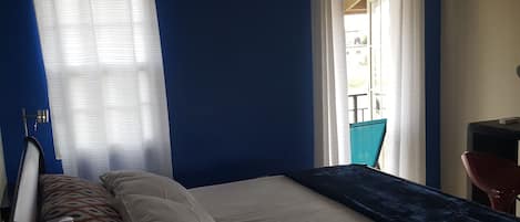 Habitación de hotel con cama, escritorio y silla. Tiene una ventana con cortinas y vistas al exterior.