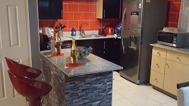 Een keuken met een granieten aanrechtblad, een stenen spatwand, een roestvrijstalen koelkast en een magnetron bovenop de koelkast.
