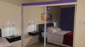 Een slaapkamer met een bed, nachtkastjes, een spiegel en een muur met een schilderij.