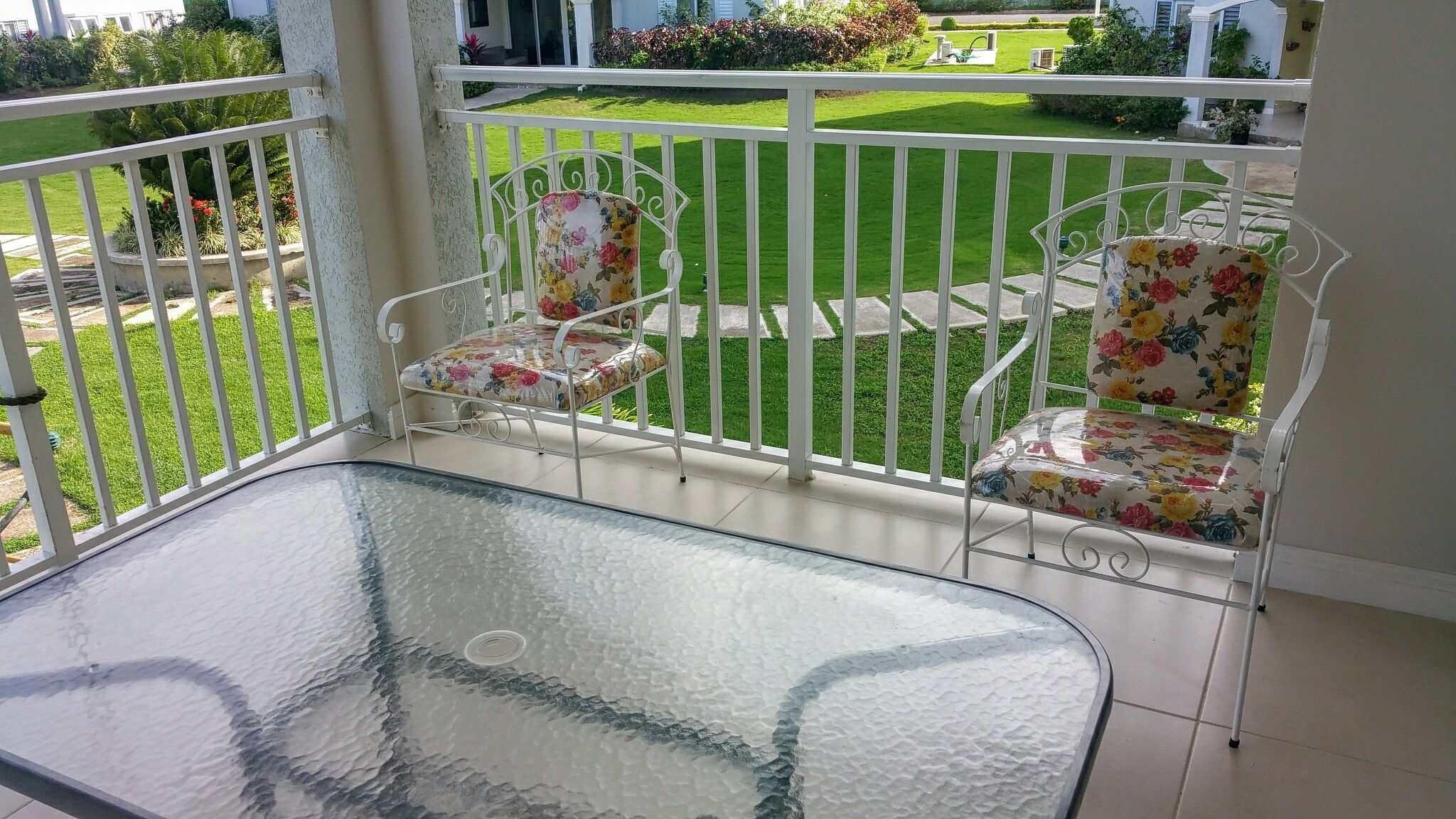 Varanda com mesa de vidro e duas cadeiras com estofamento floral.
