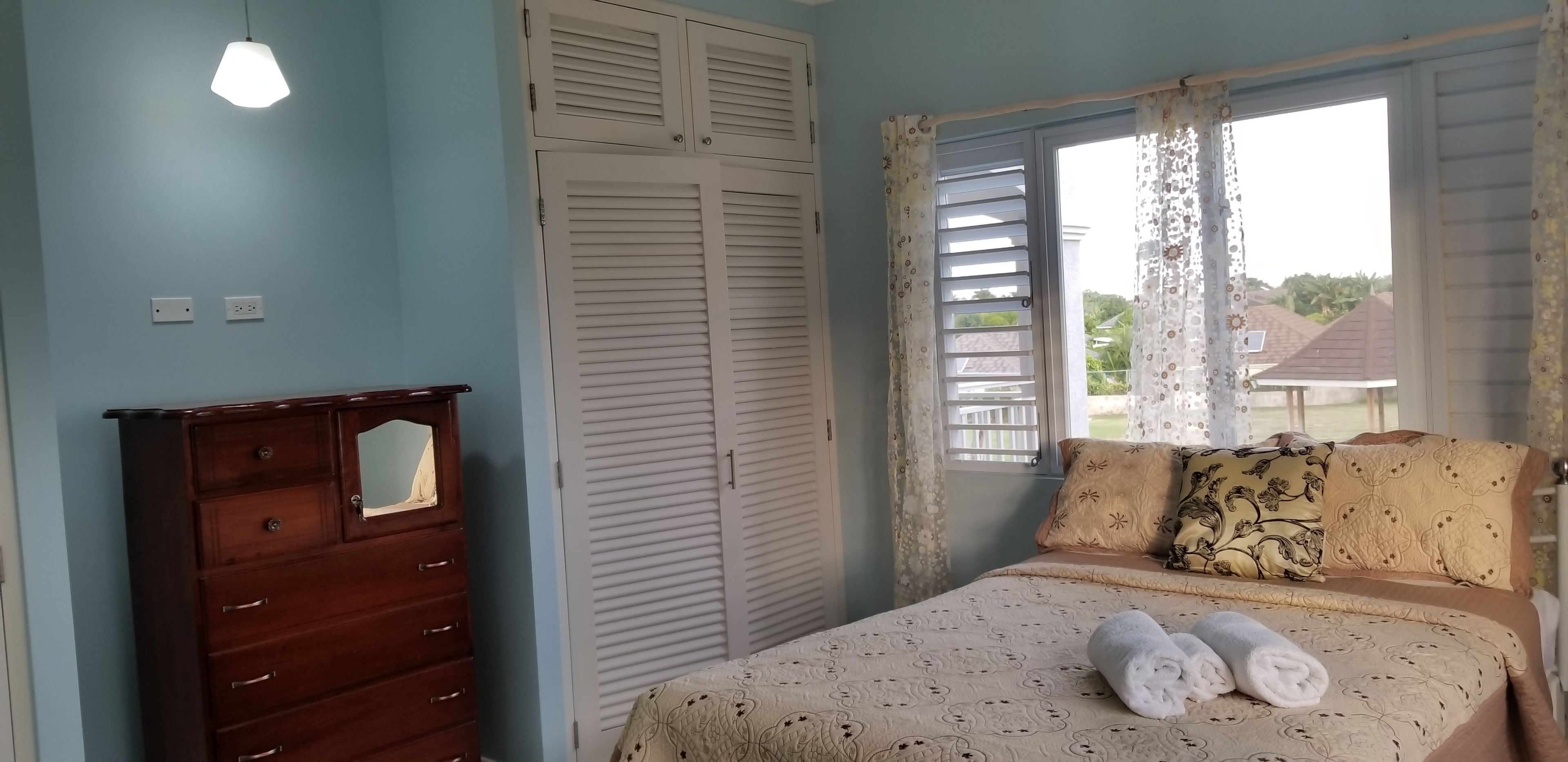 Un dormitorio con cama, cómoda, ventana con cortinas y vistas al exterior.