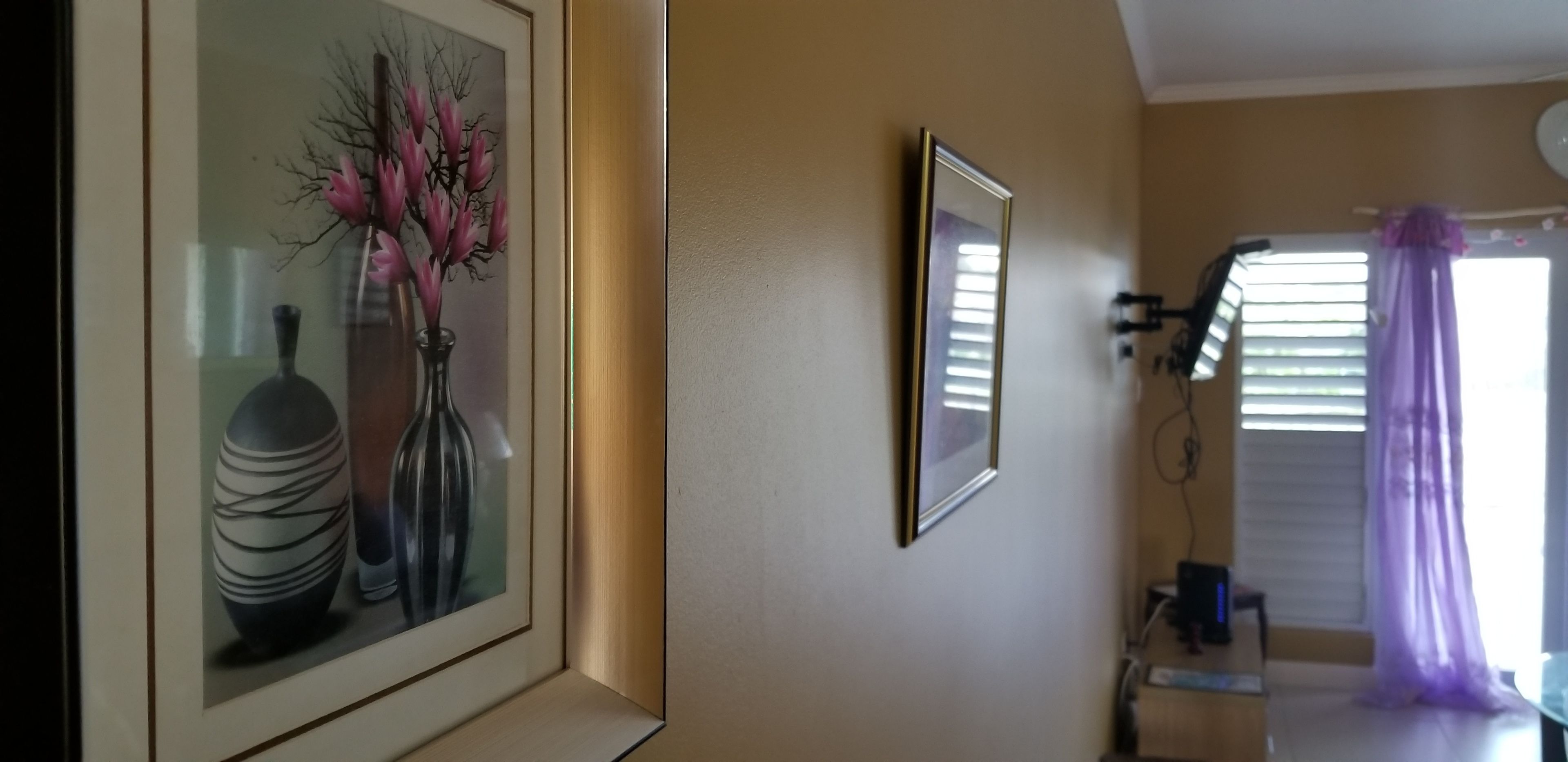 A framed artwork of vases on a wall, a mirror, and a window with blinds and curtains.