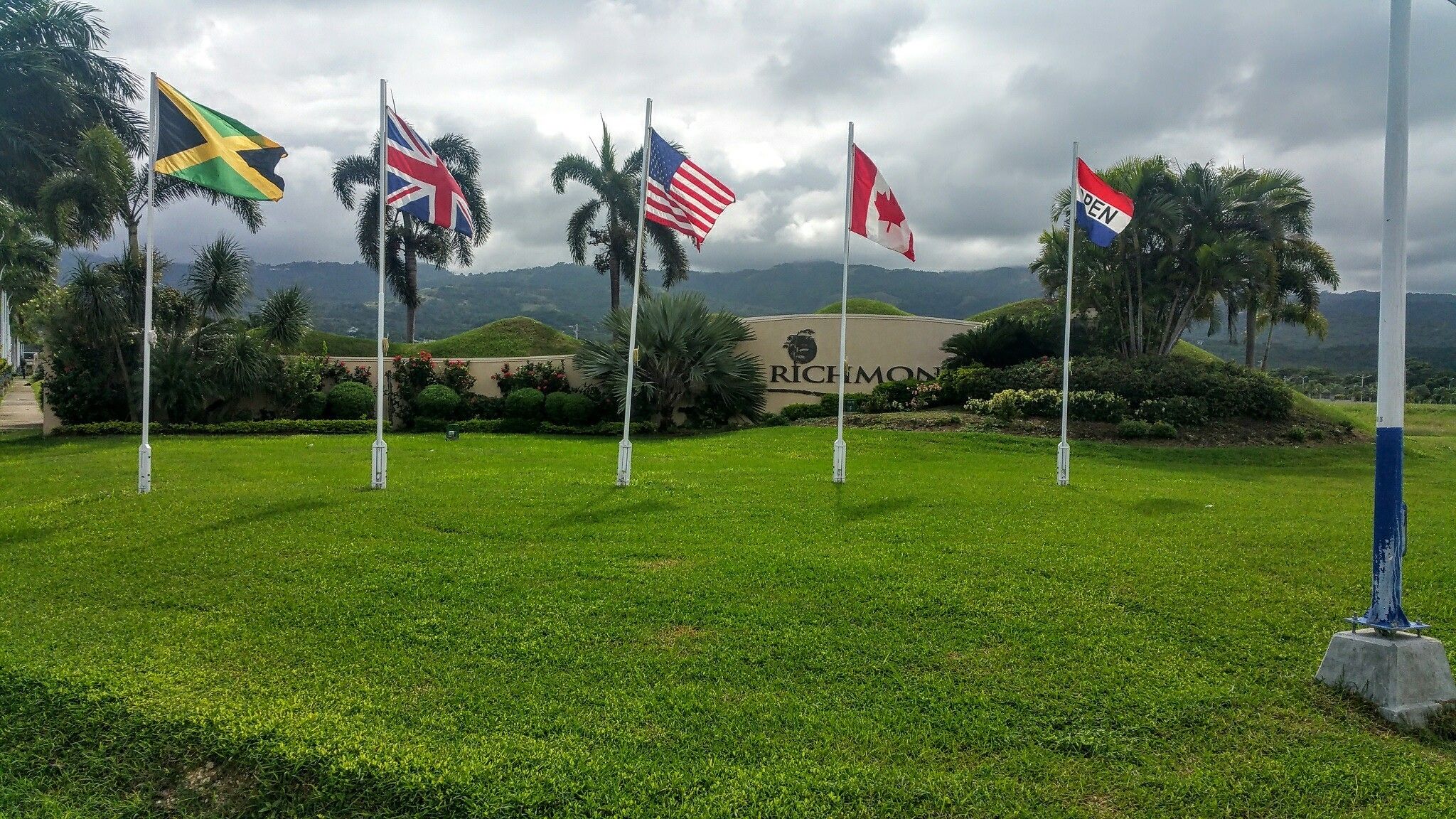Un espacio verde con varias banderas nacionales, un cartel con la palabra 'RICHMOND' y un logo, y montañas al fondo.