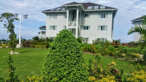 A multi-story building with a flat roof and balconies, surrounded by well-maintained gardens and a street lamp.
