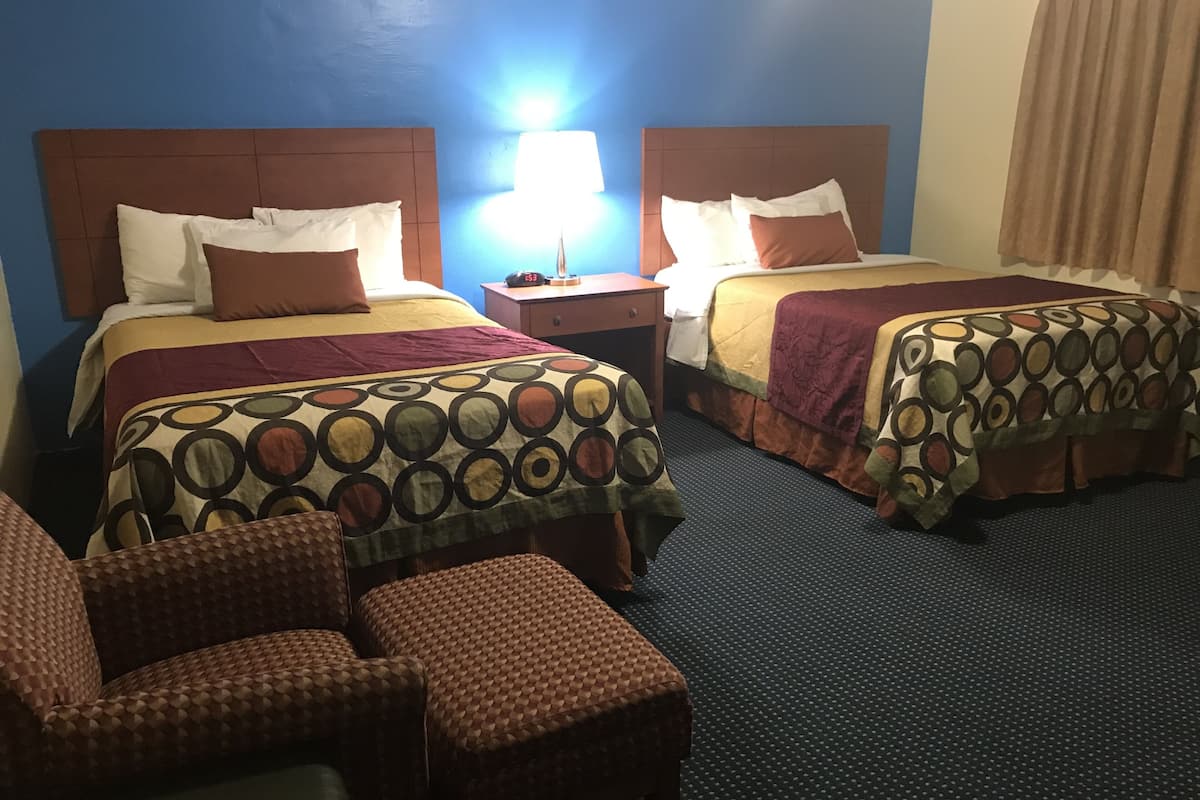 A hotel room with two beds, a nightstand, a lamp, and a seating area with chairs.