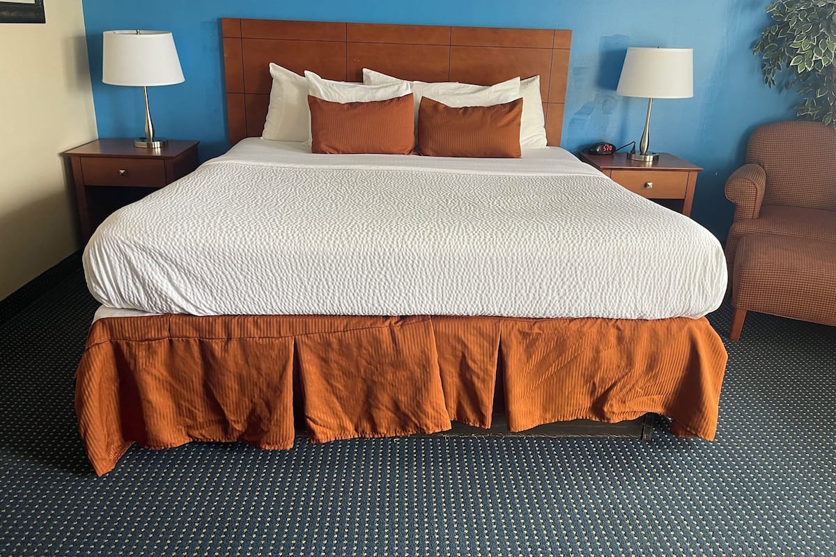 A hotel room with a large bed, two bedside tables with lamps, a chair, and a wall clock.
