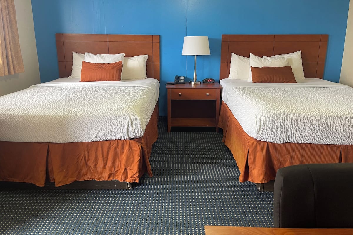 A hotel room with two beds, a nightstand with a lamp, and a small table.