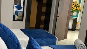 A hotel room with two beds, each with blue and white bedding, a mirror, and a door leading to a hallway with a fire extinguisher. - Hotel Casa Lamay (Bogotá)