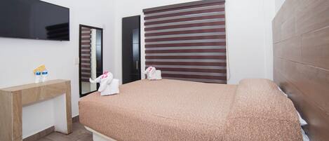 Una habitación de hotel moderna con una cama grande, una mesita de noche de madera, un televisor de pantalla plana y un ventanal grande con persianas.