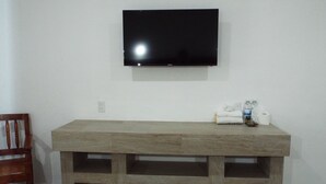 A room with a wooden desk, a flat-screen TV mounted on the wall, and a chair.