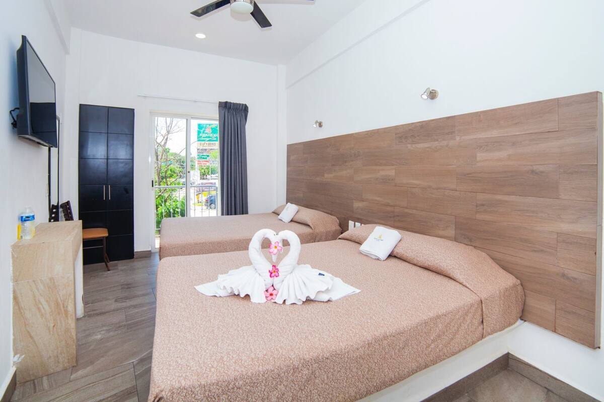 Quarto de hotel com duas camas, televisão, secretária e vista para o exterior.
