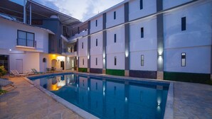 A modern building with a swimming pool, outdoor seating, and a covered area with a view of the pool.