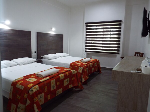 Una habitación de hotel con dos camas, un baño pequeño y un televisor montado en la pared.