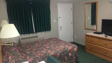Habitación de hotel con cama, escritorio, lámpara, cómoda, espejo y aire acondicionado.
