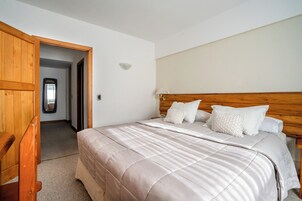 Un dormitorio con cabecera de madera, una cama grande con colcha color beige y una silla de madera.
