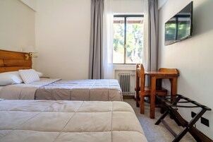 Una habitación con dos camas, un escritorio de madera, una silla, un radiador y un televisor montado en la pared.