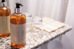 Una encimera de baño con una botella de jabón líquido y un vaso de agua.