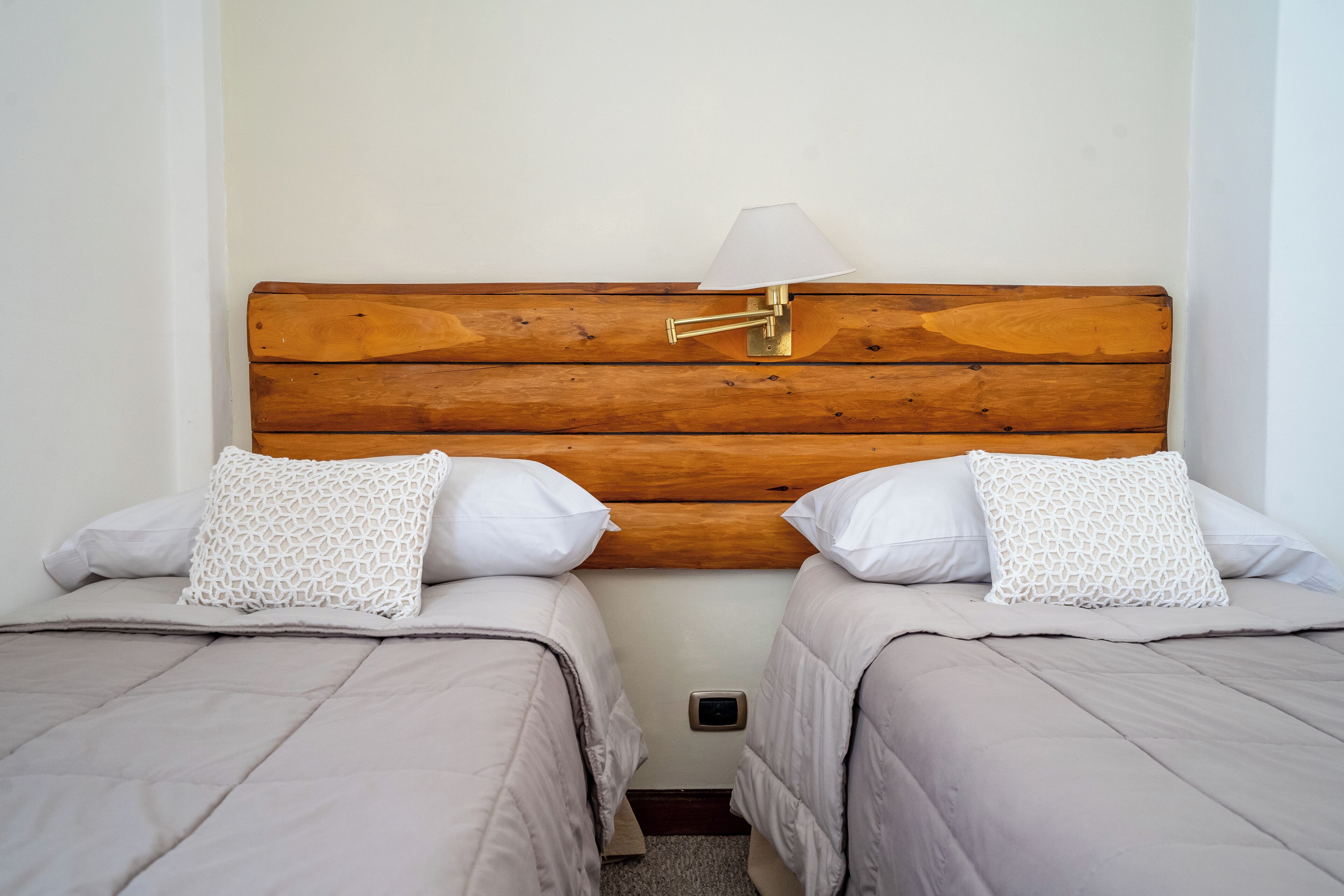 Een tweepersoonskamer met twee bedden, elk met een houten hoofdbord, witte kussens met een patroon en een nachtkastje met een lamp.