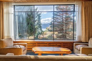 Une pièce chaleureuse avec une grande fenêtre, des meubles en bois et une vue sur les arbres et les montagnes.