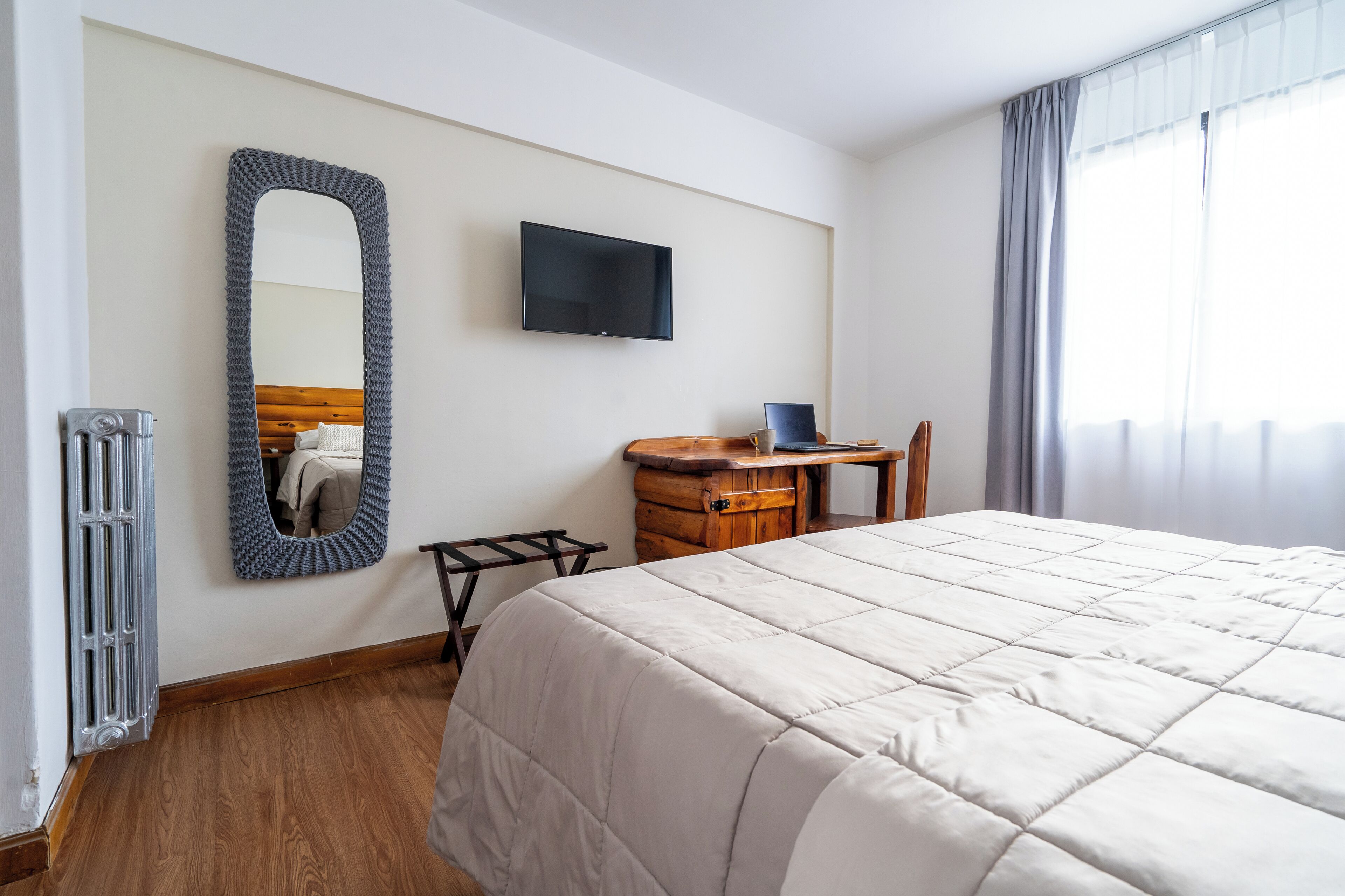 A hotel room with a large bed, a wooden nightstand, a television, and a mirror on the wall.