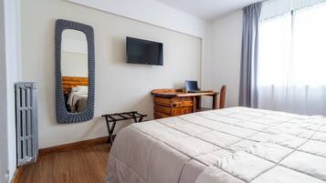 A hotel room with a large bed, a wooden nightstand, a television, and a mirror on the wall.