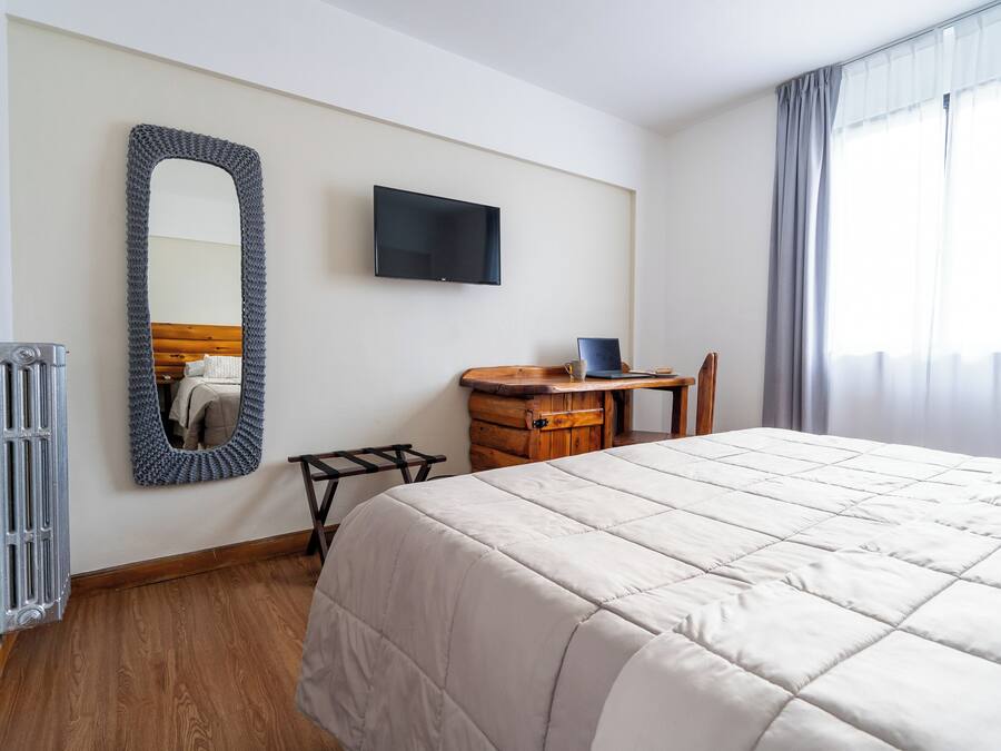 A hotel room with a large bed, a wooden nightstand, a television, and a mirror on the wall.
