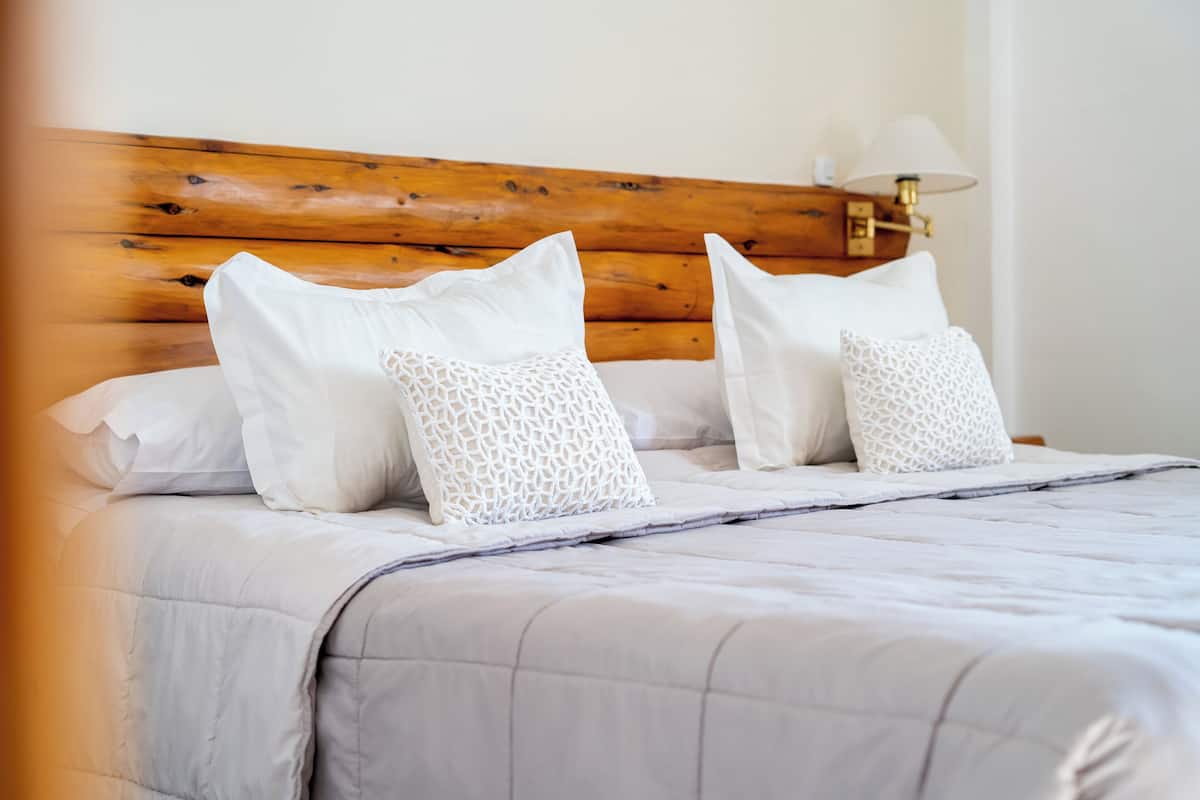 A neatly made bed with white linens and patterned pillows, a wooden headboard, and a bedside table with a lamp.