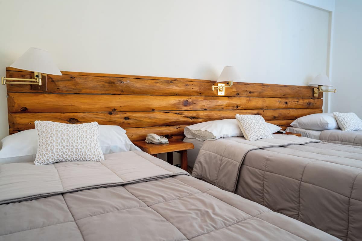 A hotel room with a wooden headboard, two beds with beige bedding, bedside lamps, and a small table with a telephone.