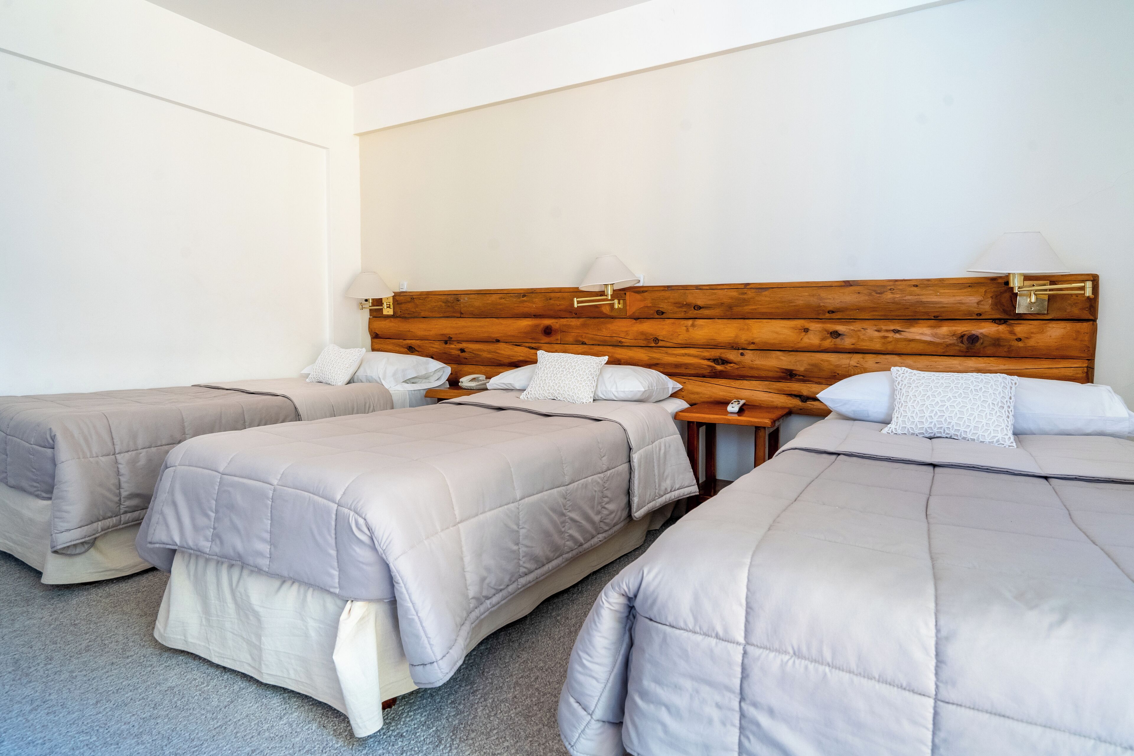 Habitación de hotel con tres camas individuales, cada una con cabecero de madera y lámparas de noche.