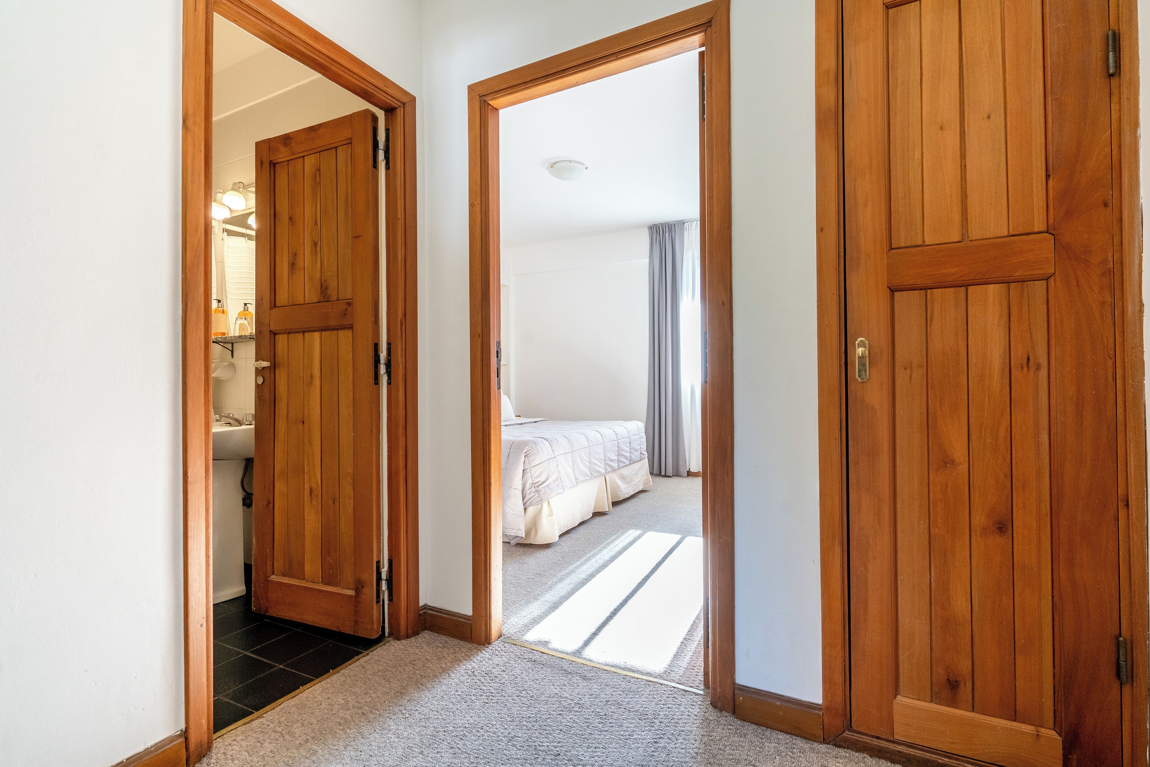 A hallway with wooden doors leading to a bathroom and a bedroom.