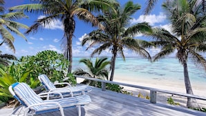Terraza de madera con dos sillones a rayas que dan a una playa con palmeras y agua turquesa cristalina.