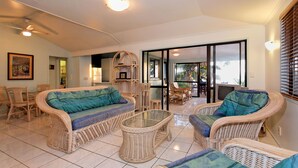 Amplia sala de estar con muebles de mimbre, una mesa de centro de cristal y vistas a un patio exterior a través de un ventanal.