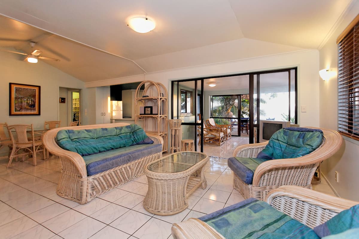 Amplia sala de estar con muebles de mimbre, una mesa de centro de cristal y vistas a un patio exterior a través de un ventanal.