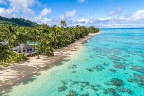A beach with clear turquoise water, palm trees, and a small house with a thatched roof. - Sands Villas Rarotonga (Rarotonga)