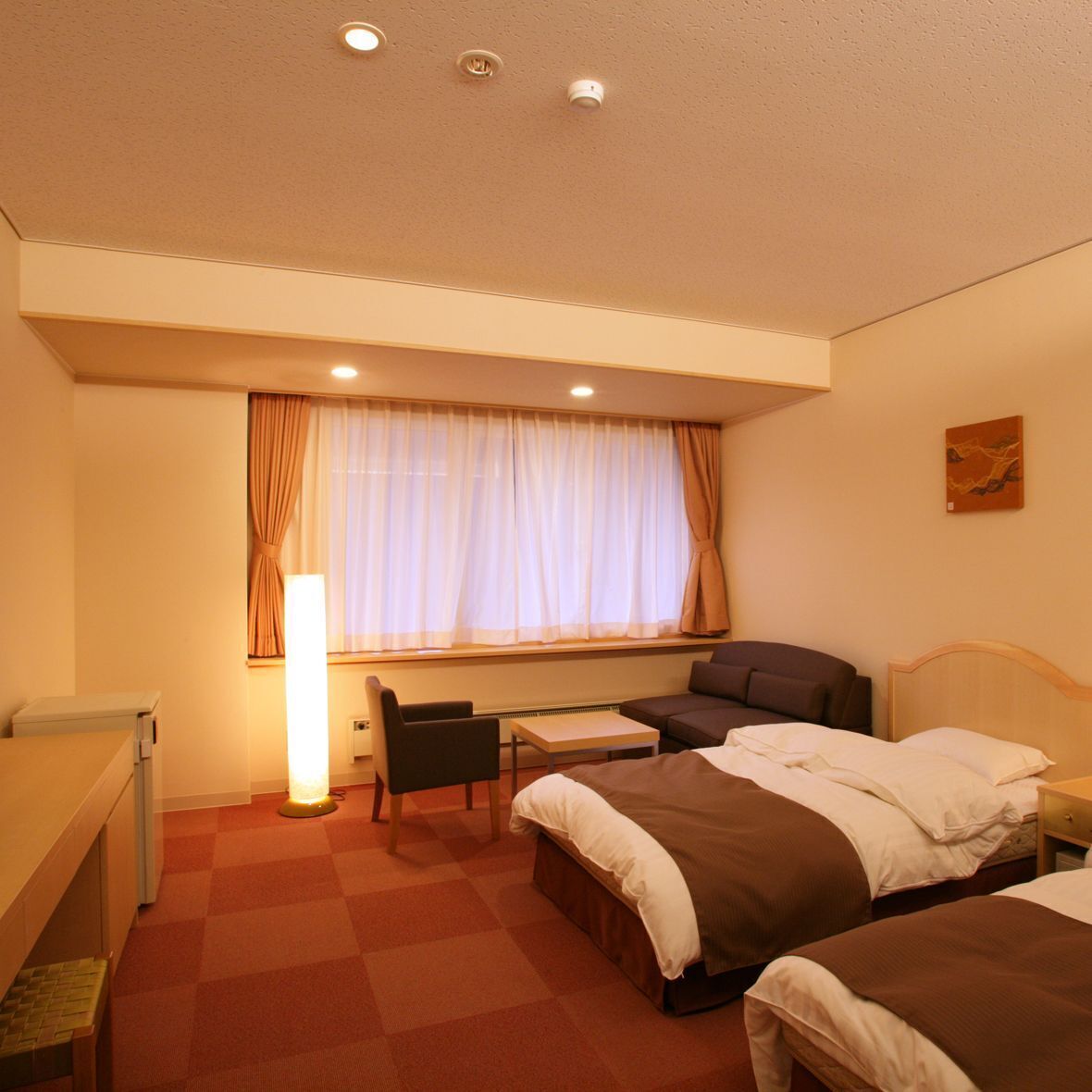 Una habitación de hotel con cama, escritorio, silla, mesa y ventana con cortinas.