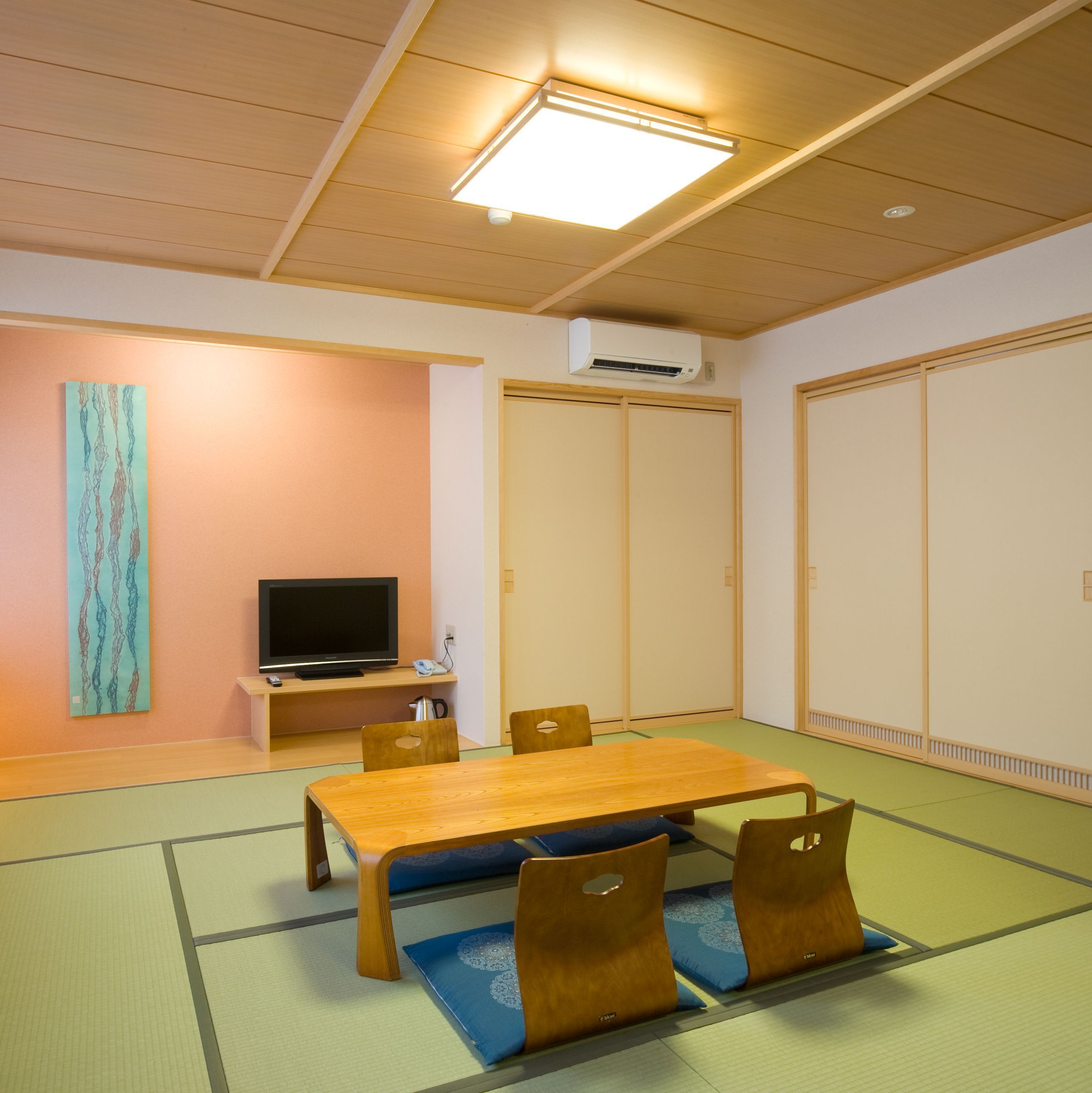 Una habitación con esteras de tatami, una mesa de madera, sillas, un televisor y una puerta corredera.