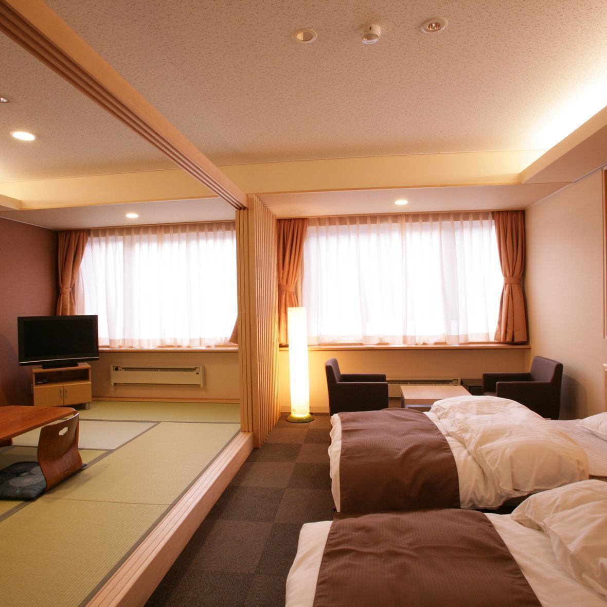 Una habitación de hotel con dos camas, un escritorio, un televisor y una ventana con cortinas.