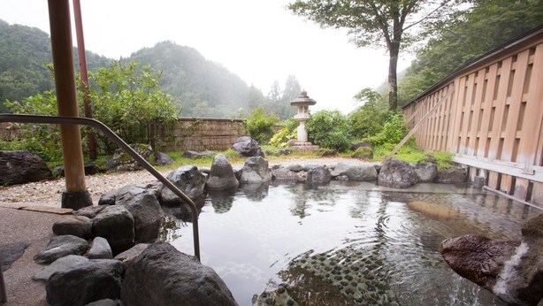 A traditional Japanese onsen with a stone bath surrounded by rocks and a wooden fence. - Gokasanso (Nanto)