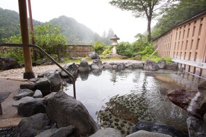A traditional Japanese onsen with a stone bath surrounded by rocks and a wooden fence.