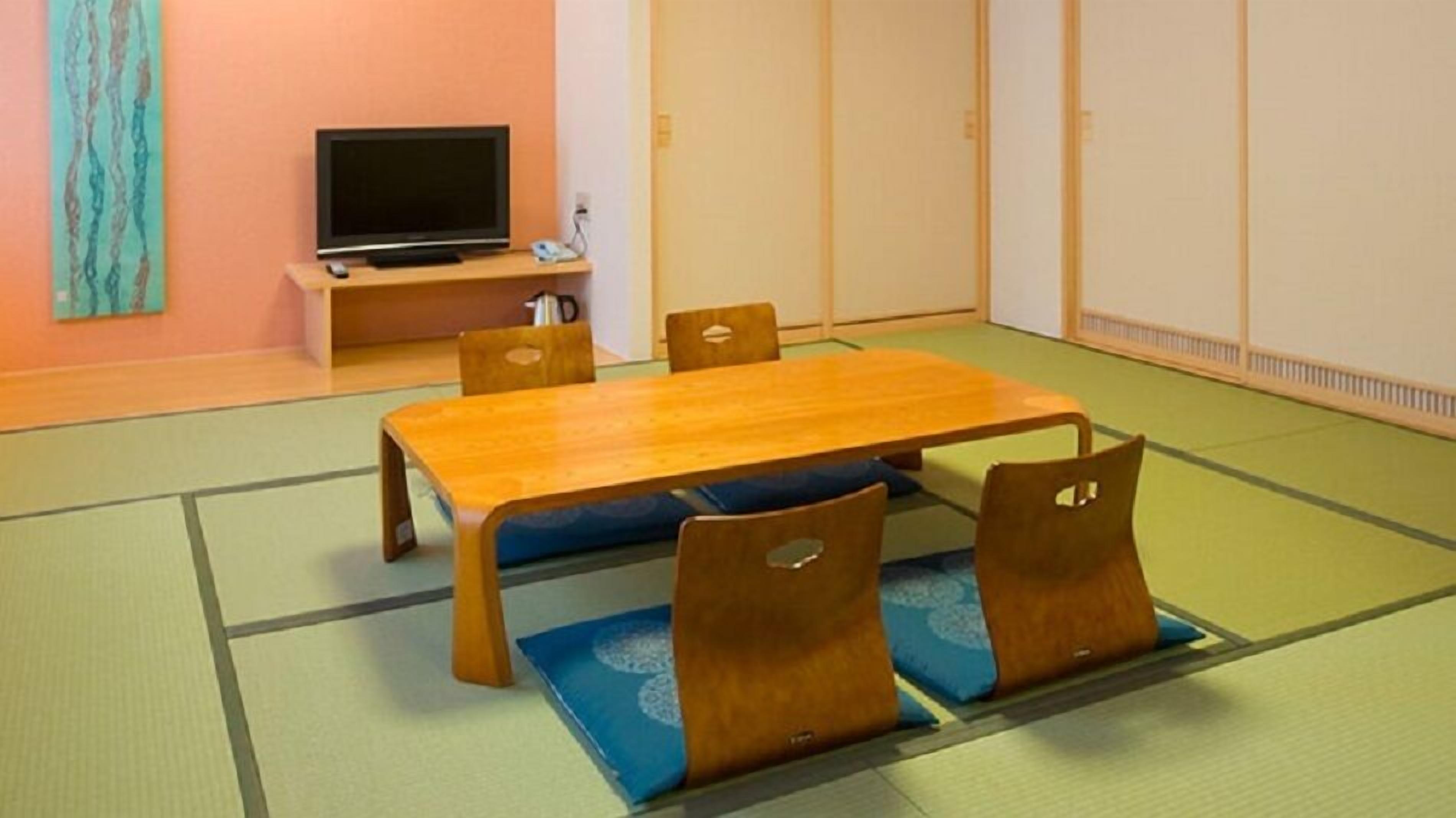 A tatami mat room with a wooden table and chairs, a television, and a sliding door.
