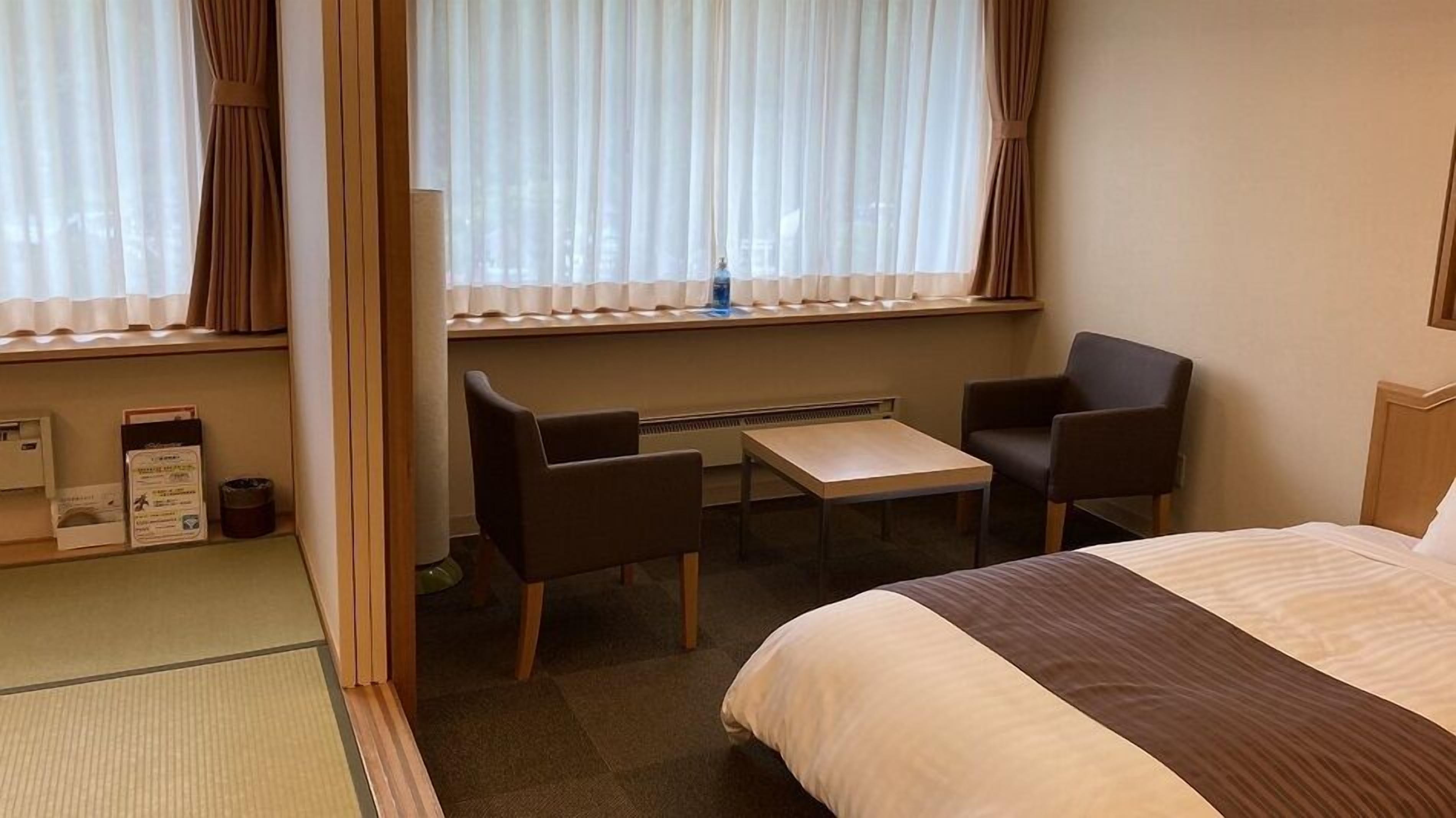 Habitación de hotel con cama, dos sillas, una mesita y ventana con cortinas.