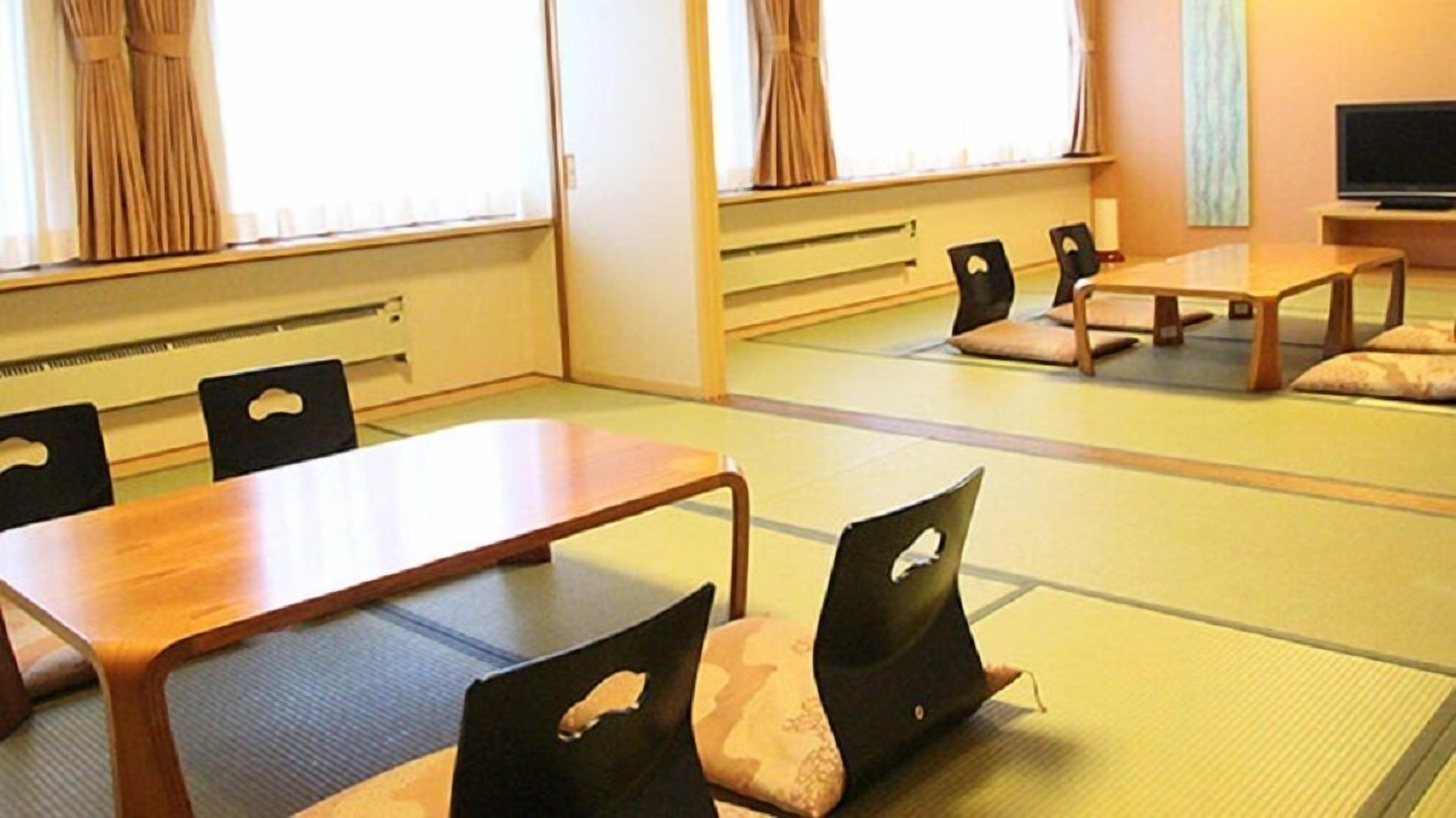 A tatami mat room with a low table and chairs, a television, and a window with curtains.