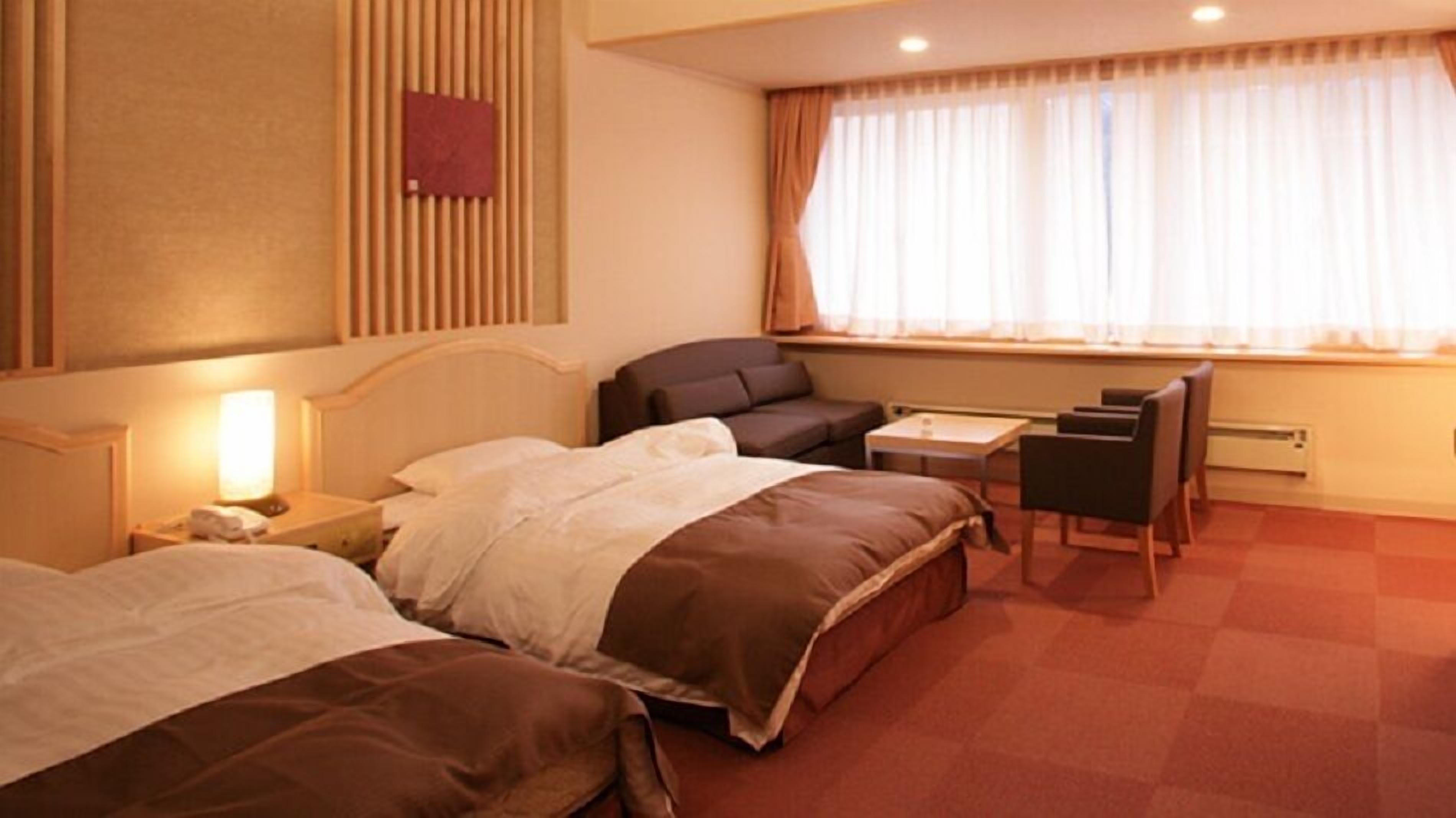 A hotel room with two beds, a desk, a chair, a lamp, and a window with curtains.