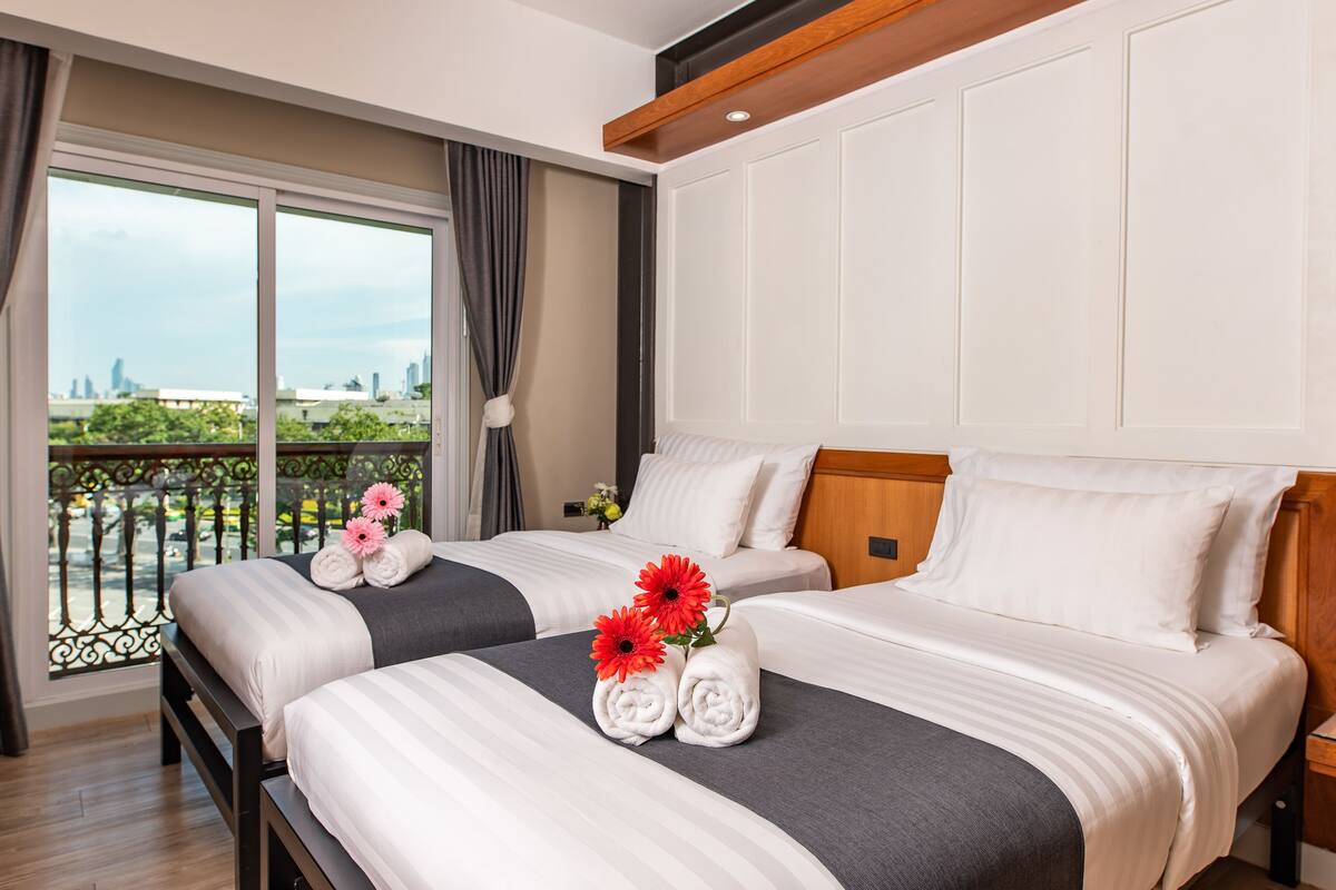 Une chambre d’hôtel avec deux lits, un balcon donnant sur la ville et une grande fenêtre avec des rideaux.