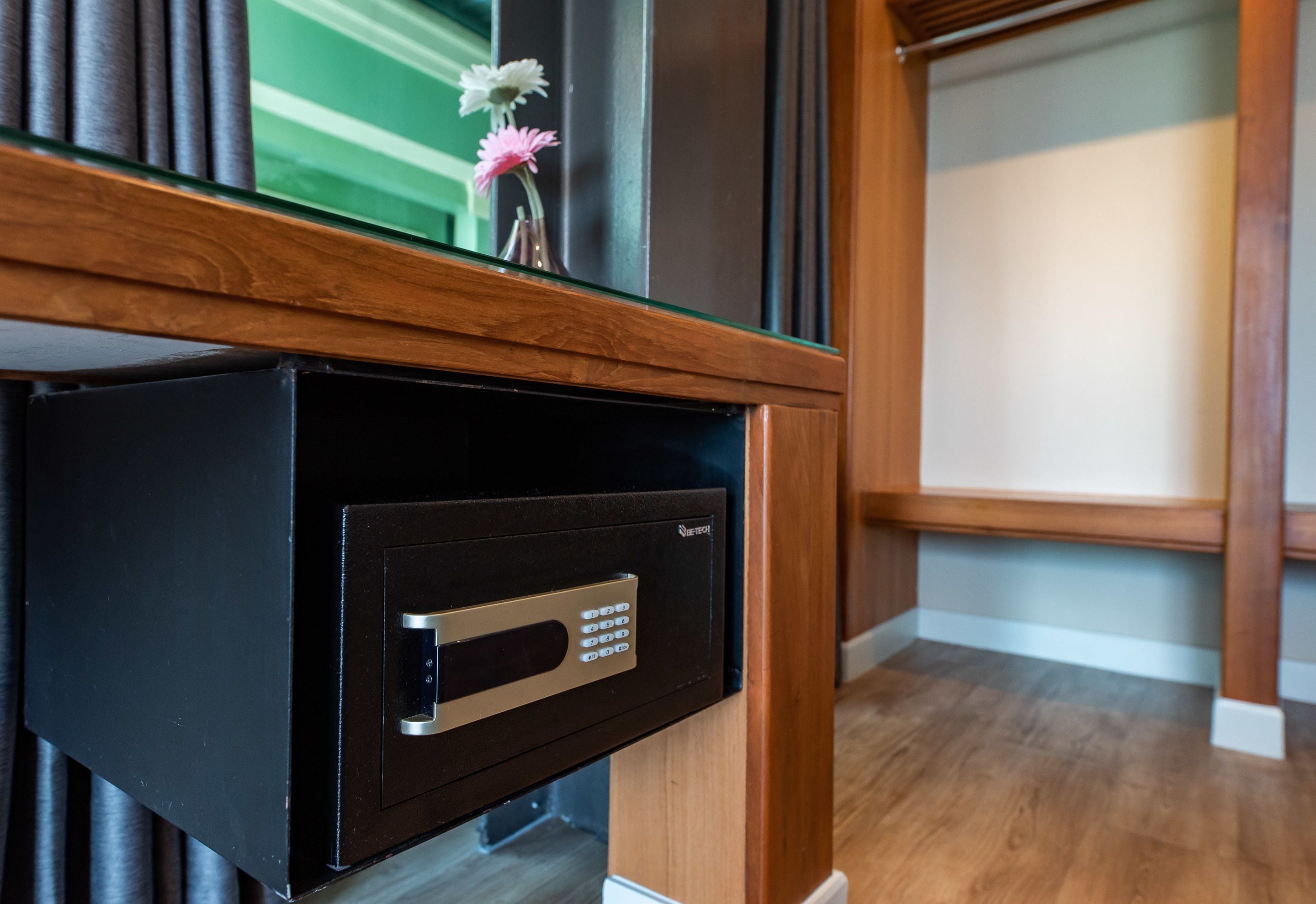 A black safe with a keypad, a wooden counter, and a small vase with flowers on top.